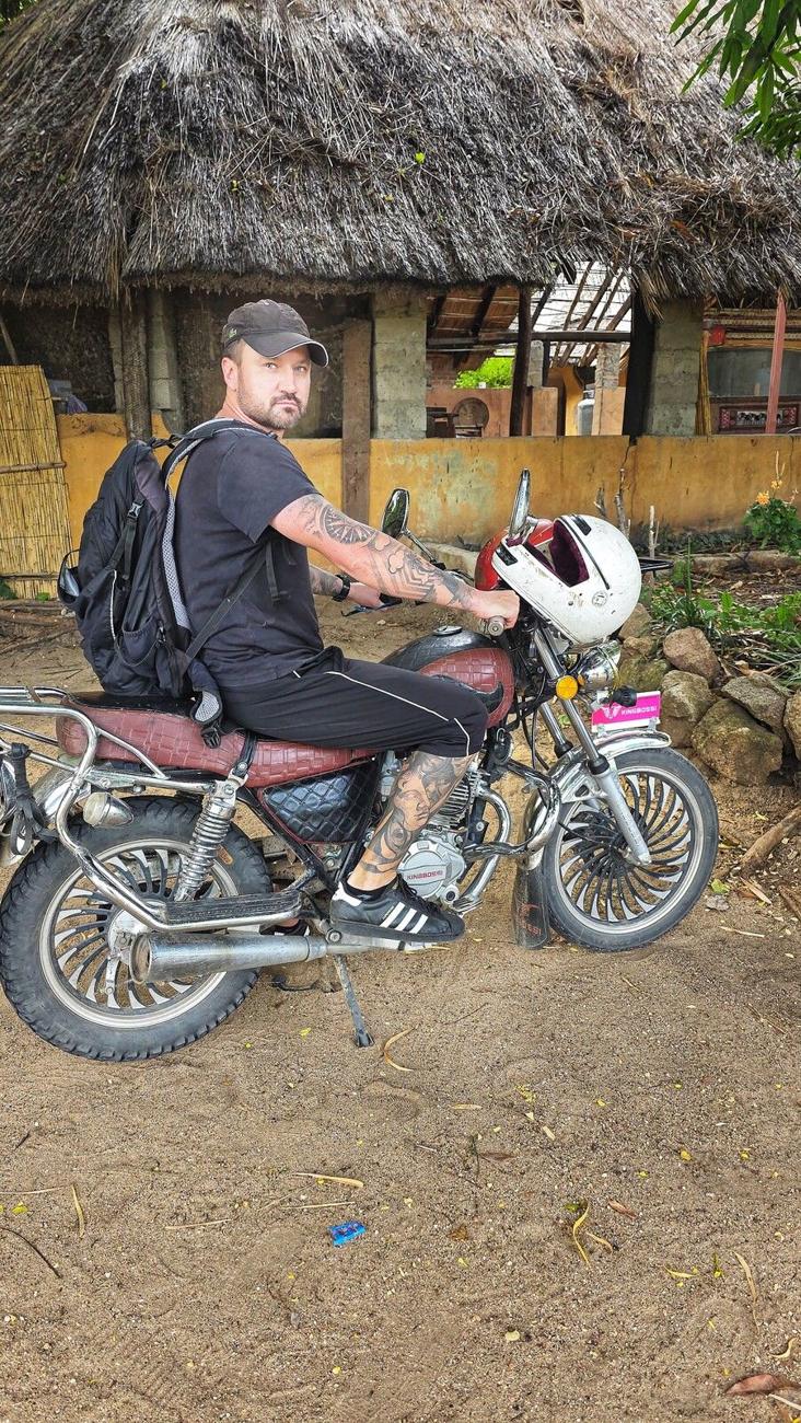 Kamil na motocyklu przed chatą krytą strzechą