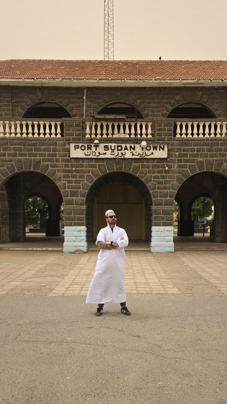 Kamil w białej galabii przed budynkiem z napisem Port Sudan